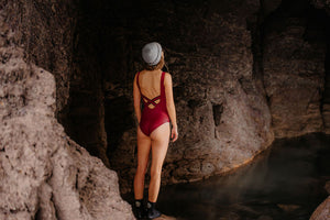Girl stood in cave wearing red swimsuit and hat before wild swimming