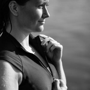 Black and white image of a woman in a short sleeve Davy J Sustainable Waterwear short sleeve swim top holding the collar and pulling up the zip