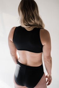 Close up of back of blonde woman in studio wearing black Davy J Sustainable Waterwear swimsuit with cut out back 