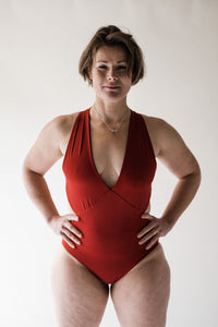 Woman in studio with short brown hair, looking powerful with hands on hips, wearing red Davy J Sustainable Waterwear cutout swimsuit with plunging neckline