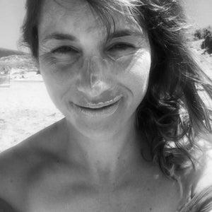 Black and white image of a lady smiling with suncream on her face sat on the beach