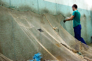 A man wearing a green t-shirt is pinning up old fishing nets to a wall 
