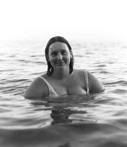 A lady with short dark hair looking into the camera smiling whilst in the sea with the water around her shoulders