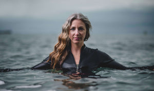 A powerful front facing image of a lady with long hair stood in the sea with the water around her shoulders.  She is wearing a black Davy J Sustainable Waterwear long sleeve swim top