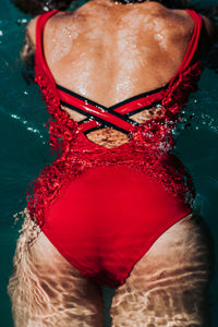A back view of a woman swimming showing the crossback detail of a red Davy J Sustainable Swimwear swimsuit