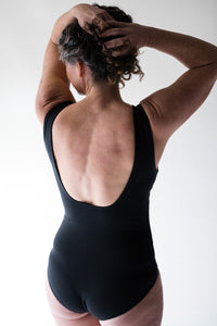 Woman in studio facing away with hands in hair wearing Davy J Sustainable Waterwear black swimsuit with low squared back