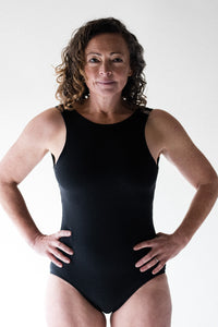 Woman in studio looking powerful with hands on hips wearing Davy J Sustainable Waterwear black swimsuit with high neck racer front