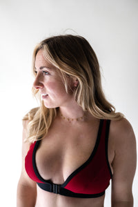 A lady with blonde hair looking to the left thoughtfully, wearing a Davy J Sustainable Waterwear red bikini top with black front opening clasp and band 