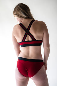A back view of a blonde lady wearing a Davy J Sustainable Waterwear red bikini top with bold crossback design and a pair of red low rise bikini briefs with black waistband