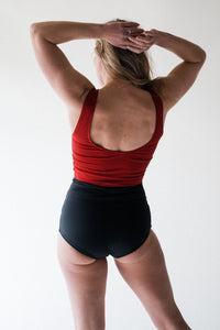 A back view of a blonde lady with her arms in the air, wearing a Davy J Sustainable Waterwear red cropped swim top with scoop back and shoulder straps.  She also wears a pair of black high waist bikini briefs