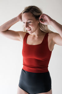 Blonde smiling woman in studio with hands in hair wearing Davy J Sustainable Waterwear red crop swim top and black high waist bikini briefs rolled down to show red lining