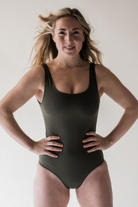 Smiling blonde woman in studio looking powerful with hands on hips wearing Davy J Sustainable Waterwear olive classic crossback swimsuit 