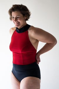 Smiling woman with short brown hair and hands on hips in studio wearing Davy J Sustainable Waterwear red halter swim top with black collar overlapping black high waist bikini briefs 