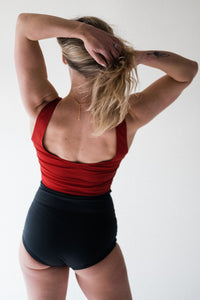 Woman in studio facing away with hands in her blonde hair wearing Davy J Sustainable Waterwear red crop swim top with scoop back overlapping black high waist bikini briefs 