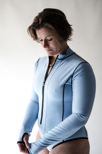 A woman with short brown hair looks down at the sleeve detail of a Davy J Sustainable Waterwear powder blue long sleeve swimsuit pulled down over her hand.