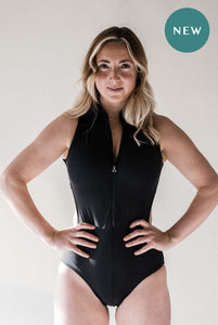 A lady with blonde hair standing in a strong stance with her hands on her hips, looking straight into the camera wearing a black Davy J sustainable waterwear swimsuit