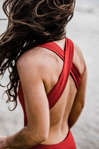Close up of back of woman with long wavy hair blowing in the wind wearing red Davy J Sustainable Waterwear cutout swimsuit with wide cross back straps
