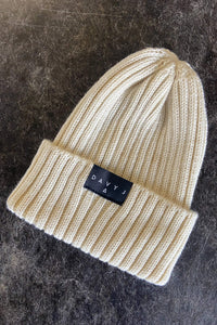 Flat lay image of Davy J Sustainable Waterwear cream merino wool beanie with turn up.  A black label with the Davy J logo in white text is sewn to the top of the turn up.   