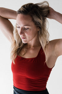 A blonde lady holding back her hair, wearing a red Davy J sustainable swimwear body swim top