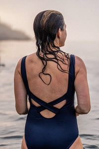 Woman with wet hair stood in the sea looking to the horizon wearing Davy J Sustainable Waterwear navy classic swimsuit with cross back