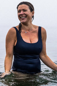 Laughing woman stood in the sea wearing Davy J Sustainable Waterwear navy classic cross back swimsuit and silver necklace 